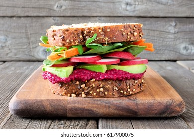 Superfood sandwich with beet hummus, avocado, vegetables and greens, on whole grain bread against a wooden background