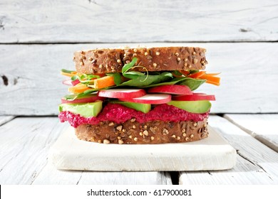 Superfood Sandwich With Beet Hummus, Avocado, Vegetables And Greens, On Whole Grain Bread Against A White Wood Background