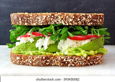 Superfood Sandwich With Whole Grain Bread, Avocado, Egg Whites, Radishes And Pea Shoots On Marble Against A Black Background