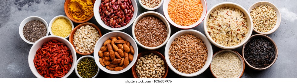 Superfoods and cereals selection in bowls: quinoa, chia, goji berry, mung bean, buckwheat, bean, turmeric, polba, bulgur, lentil, sesame, flax seed, wild rice, almond on grey concrete background