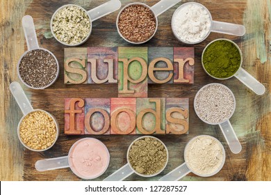 superfoods word in letterpress wood type surrounded by plastic scoops of healthy seeds and powders (chia, flax, hemp, pomegranate fruit powder, wheatgrass, whey protein, maca root) - top view