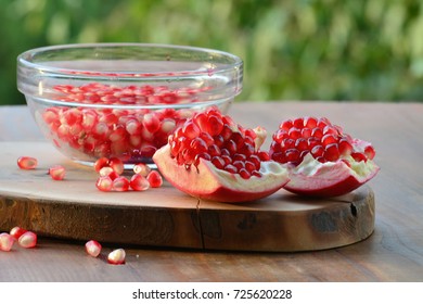 Superfruit, peeled open pomegranate and red seeds in glass bowl over wooden table (Punica granatum)