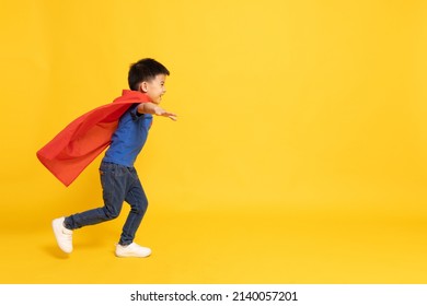 Superhero Asian boy in red cape running isolated yellow background, Full body composition