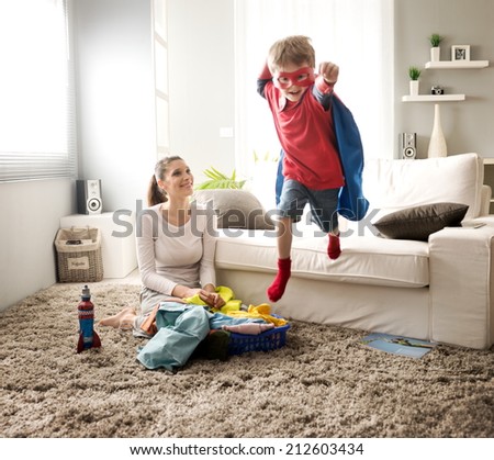 Superhero boy and his mother doing laundry together in the living room.