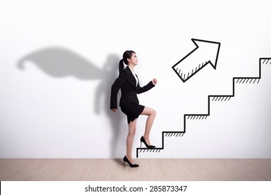 Superhero Business Woman Stepping Up On Stairs To Gain Her Success With White Wall Background, Asian