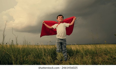 Superhero child playing against sky in park. Little boy hero in red cloak look into sky. Boy kid plays superhero in red cape, childhood dream. Brave child winner dream in red raincoat plays in nature - Powered by Shutterstock