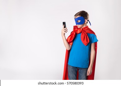 Superhero Child Using Mobile Phone. Superman Kid In Red Cape And Blue Mask.