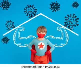 Superhero Child Wearing Protective Mask  Indoor. Portrait Of Super Hero Kid Against Blue Paper Background. Stay Home And Social Isolation Concept