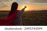 Superhero girl playing at sunset. Teen girl play in red cape against sun sky. Brave superhero woman meets day dawn. Girl dream in red cape in park. Red superhero costume. Flight imagination in nature