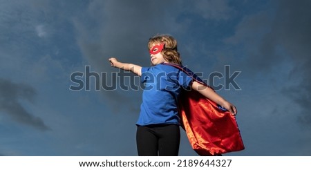 Superhero kid against dramatic blue sky background. Strong super hero boy with super power.