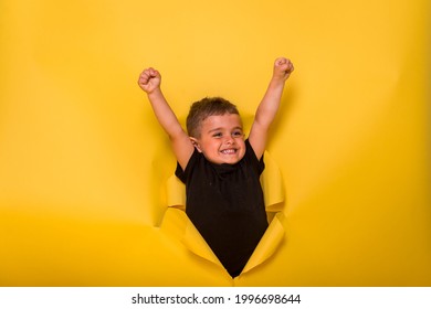 Superhero kid breaking through yellow paper wall. Winner superhero child boy ready to go to kindergarten. Back to school. Hero little boy with raised hands