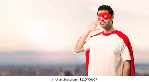 Superhero man with mask and red cape listening to something by putting hand on the ear on a sunset background - Shutterstock ID 1110406637