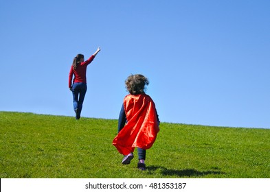 Superhero Mother Show Her Daughter How To Be  A Superhero Against Blue Sky Background With Copy Space. Concept Photo Of Super Hero, Girl Power, Play Pretend, Childhood, Imagination. Real People