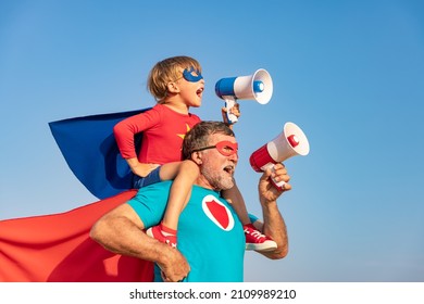 Superhero senior man and child playing outdoor. Super hero grandfather and boy shouting through loudspeaker against blue summer sky background. Family holiday concept. Happy Father's day - Powered by Shutterstock