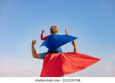 Superhero senior man and child playing outdoor. Super hero grandfather and boy having fun together against blue summer sky background. Family holiday concept. Happy Father's day. Rear view portrait