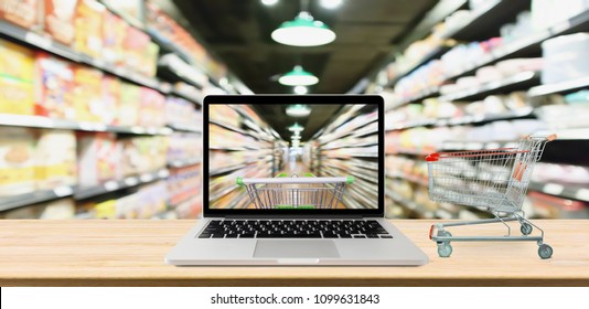 supermarket aisle blurred background with laptop computer and cart on wood table online shopping concept