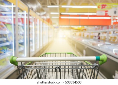 Supermarket aisle with empty green shopping cart       