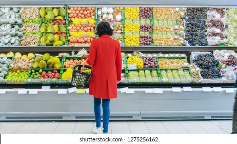 At The Supermarket: Alone Woman Chooses Organic Fruits In The Fresh Produce Section Of The Store. She Picks Up Cantaloupe And Puts Them Into Her Shopping Basket. Back View Shot.