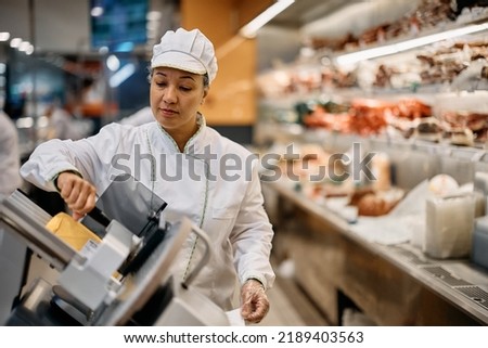 Supermarket clerk using slicer while working at delicatessen section.