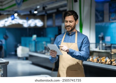 Supermarket employee in apron using digital tablet for inventory management. Image represents technology in retail, efficiency, and modern grocery store environment. Fresh produce and vibrant setting - Powered by Shutterstock