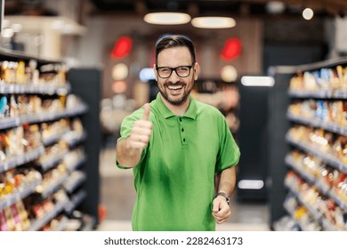 A supermarket employee is standing at marketplace and giving thumbs up while smiling at the camera. - Powered by Shutterstock