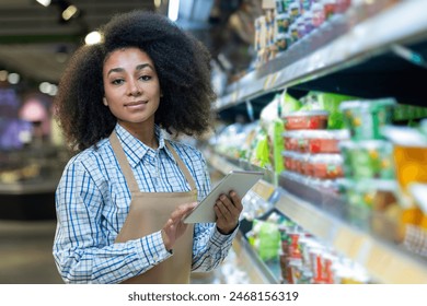 A supermarket employee with a tablet in hand, working and managing the products on the aisle shelves. - Powered by Shutterstock