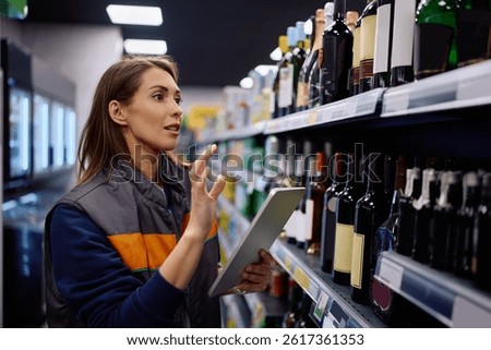 Supermarket employee using touchpad while checking stock of supplies on shelves. 