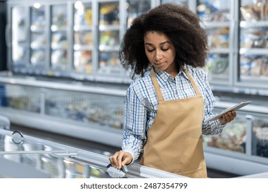 Supermarket employee wearing apron cleaning freezer aisle while holding clipboard in grocery store. Represents cleanliness, organization, customer service. Ideal for retail supermarket - Powered by Shutterstock