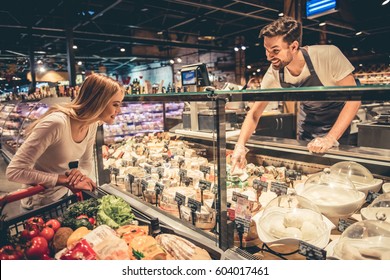 At the supermarket. Handsome worker is offering cheese to the beautiful customer and smiling - Powered by Shutterstock