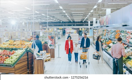 At the Supermarket: Happy Family of Three, Holding Hands, Walks Through Fresh Produce Section of the Store. Father, Mother and Daughter Having Fun Time Shopping. High Angle Panoramic Shot.