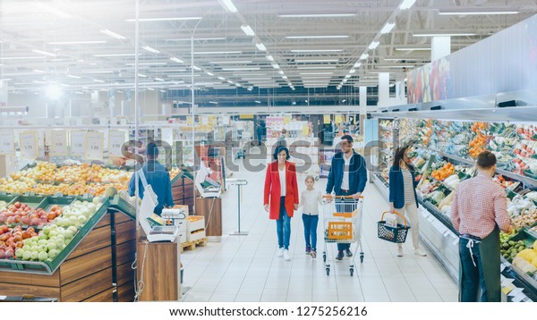 At the Supermarket: Happy Family of Three, Holding\
Hands, Walks Through Fresh Produce Section of the Store. Father,\
Mother and Daughter Having Fun Time Shopping. High Angle Panoramic\
Shot.