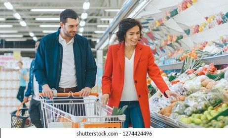 At the Supermarket: Happy Young Couple Chooses Organic Vegetables in the Fresh Produce Section of the Store. Boyfriend Pushes Shopping Cart while Girlfriend Picks up Groceries. - Powered by Shutterstock