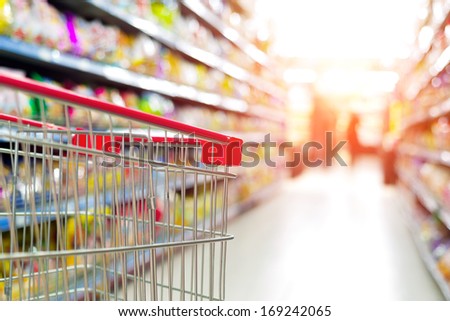 Supermarket interior, empty red shopping cart.
