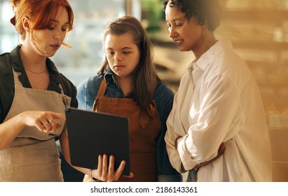 Supermarket Manager Using A Digital Tablet While Having A Discussion With Her Employees In A Staff Meeting. Group Of Diverse Women Working Together In An All-female Small Business.