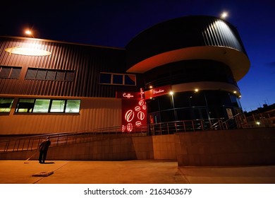 Supermarket Novomariinsky, City Of Anadyr, Chukotka, Russia - October 9,2008. Night View Of The Shopping Center. A Janitor Is Sweeping The Street Near The Building. Cafe Sign On The Front Of The Store