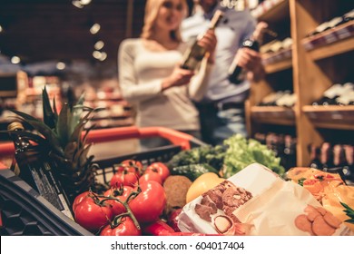 At the supermarket. Shopping cart full of goods, in the background young couple choosing wine - Powered by Shutterstock