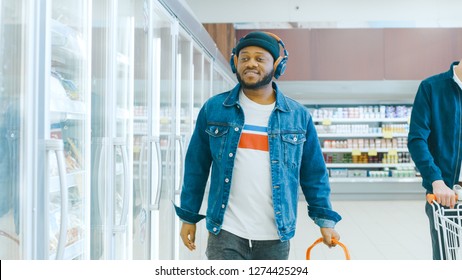 At The Supermarket: Stylish African American Guy With Headphones Walks Through Frozen Goods Section Of The Store.