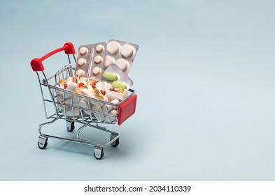 A Supermarket Trolley Full Of Blister Pills, A Lot Of Pills In A Wheelbarrow. Concept: Home Delivery Of Medicines.Empty Space, Place For Text, Poster, Board.
Medical Blue Background.