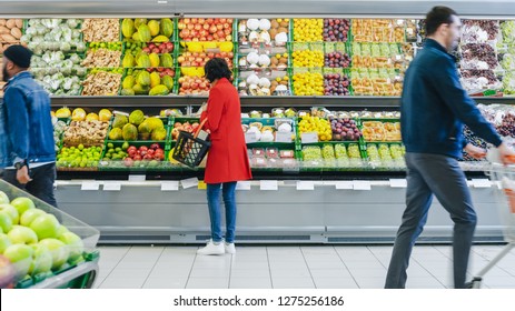 At The Supermarket: Woman Chooses Organic Fruits In The Fresh Produce Section Of The Store. She Picks Up Cantaloupe And Puts Them Into Her Shopping Basket. Back View Shot.