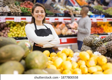 Supermarket woman worker in black apron putting melons in his department - Shutterstock ID 1877800558