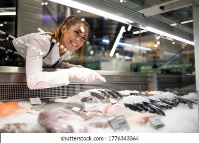 Supermarket worker arranging frozen fish for sale.Woman in working uniform selling fish in grocery store.  - Powered by Shutterstock