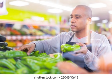 Supermarket Worker In Black Apron Putting Vegetables In His Department