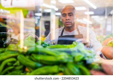 Supermarket Worker In Black Apron Putting Vegetables In His Department