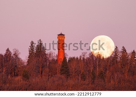 Supermoon going down by a tower at dawn