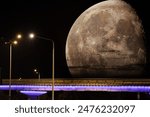 The supermoon rises above the horizon. Photo collage of a huge Moon over a road bridge with street lights at night