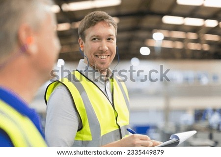 Supervisor with clipboard smiling at worker in steel factory