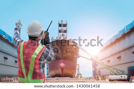 Supervisor in command repairing control worker by walkie - talkie in hand holding during Big ship under repairing or maintenance on floating dry dock in shipyard.