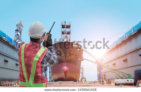 Supervisor in command repairing control worker by walkie - talkie in hand holding during Big ship under repairing or maintenance on floating dry dock in shipyard.
