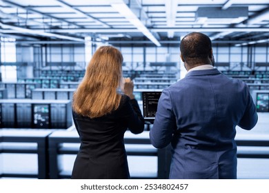 Supervisor inspecting server hub, making sure rigs are functioning optimally. Employee showing overseeing inspector recovery plan on laptop, monitoring energy consumption