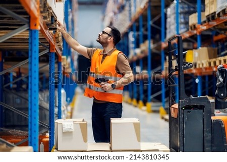 A supervisor with scanner in hands checking on goods in boxes in storage.